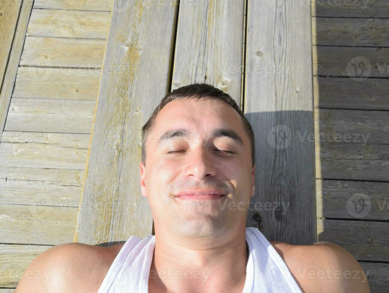 homme est mensonge sur une banc et élongation. une sourire sur le visage de une homme mensonge sur une banc. photo