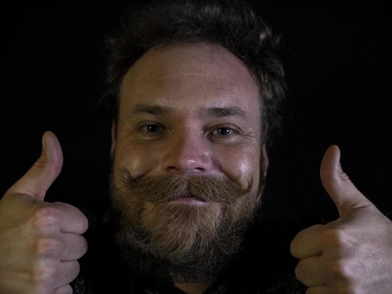 visage drôle d'un homme avec une barbe et une moustache et montrant les pouces vers le haut photo