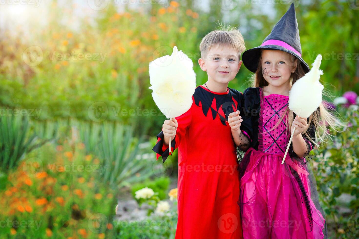 peu garçon et fille dans costumes de une sorcière et un bourreau pour Halloween. les enfants en portant coton bonbons. photo