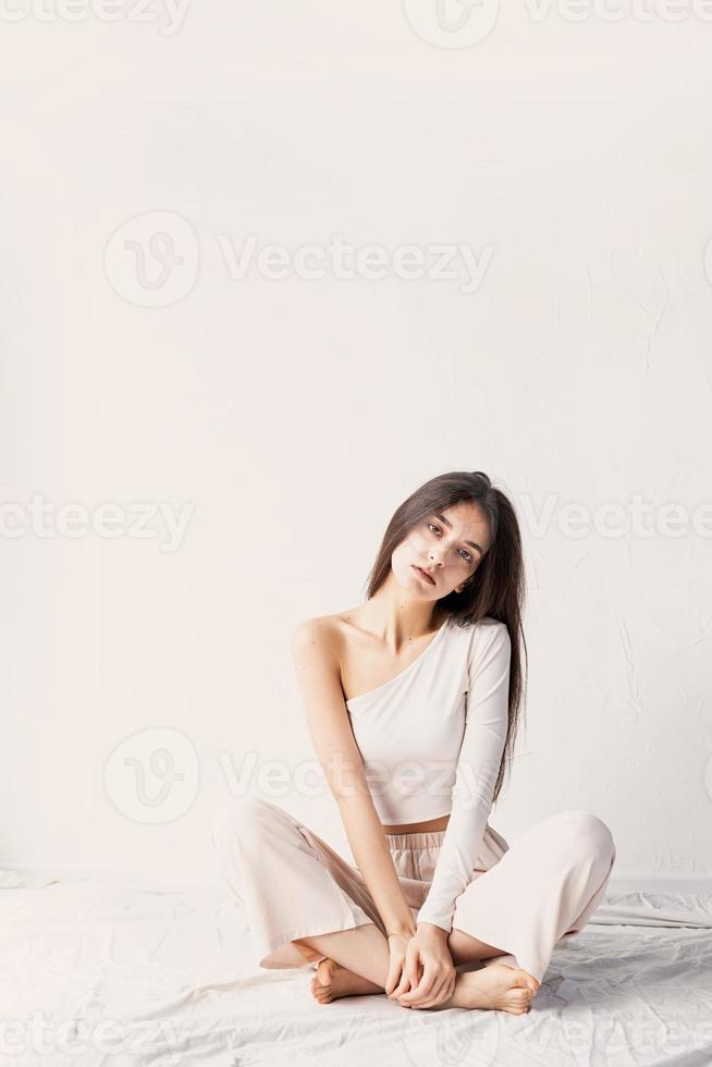 belle jeune femme dans des vêtements confortables blancs assis sur le sol photo
