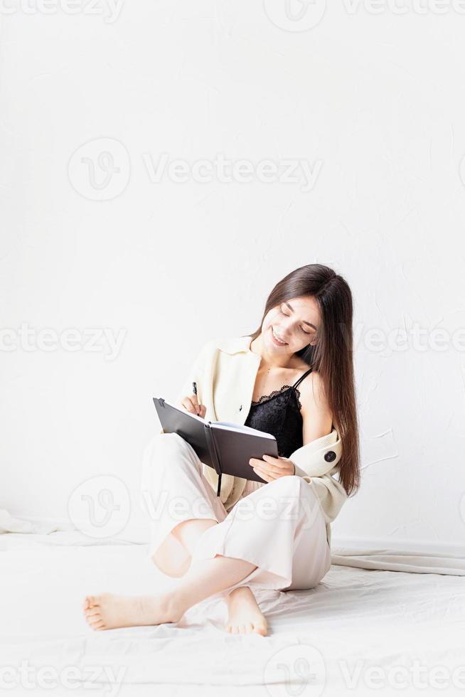 femme dans des vêtements confortables à la maison écrivant des notes assis sur le sol photo