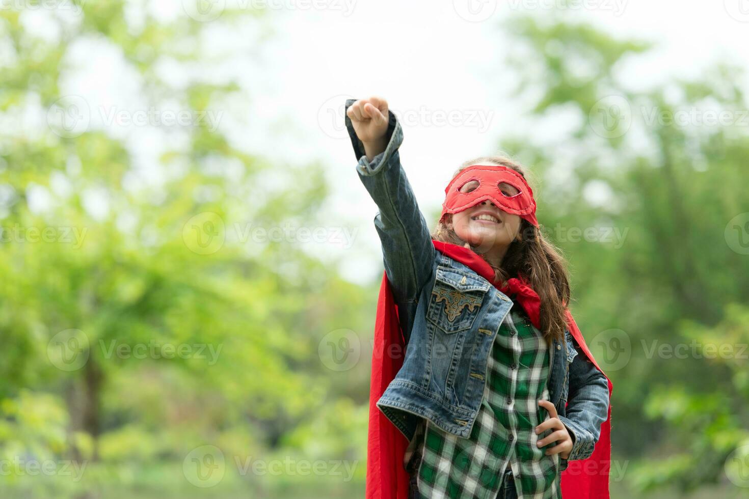 sur une magnifique journée dans le parc, une Jeune fille jouit sa vacances. espiègle avec une rouge super-héros costume et masque. photo