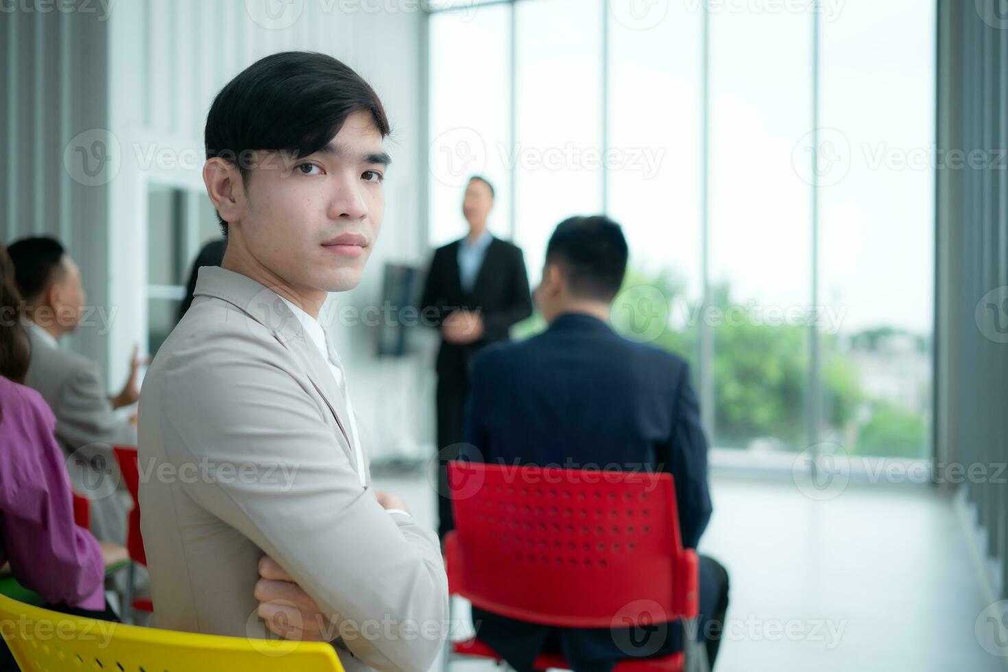 portrait de une Jeune asiatique homme d'affaire séance derrière une séminaire pièce avec une collègue dans le premier plan écoute à le conférence photo