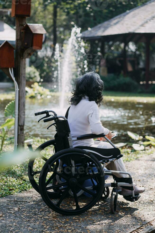 asiatique Jeune femme infirmière à allaitement Accueil prendre se soucier désactivée Sénior homme. soignant médecin servir physique thérapie pour plus âgée personnes âgées patient à exercice et entraine toi en marchant sur marcheur ou canne à cour. photo