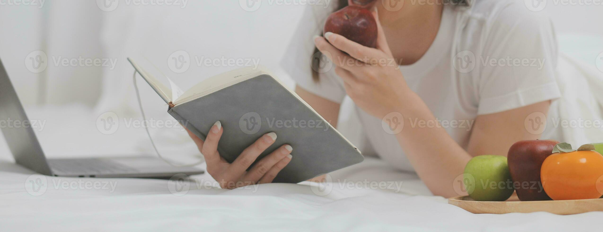 efficace Jeune millénaire fille séance sur une lit dans le matin, les usages portable ordinateur et mange des croissants et les boissons café pour petit déjeuner photo