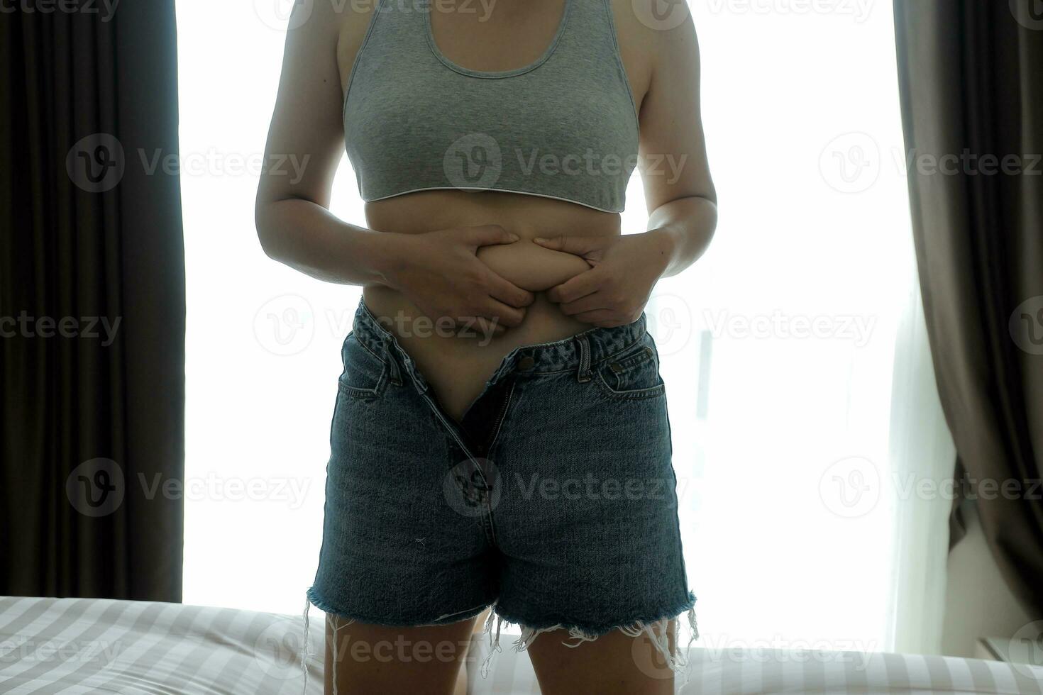 proche en haut de une ventre avec cicatrice de césarienne et abdominal graisse. aux femmes santé. une femme habillé en haut dans tenue de sport démontrant sa imparfait corps après une accouchement avec garderie sur le Contexte. photo