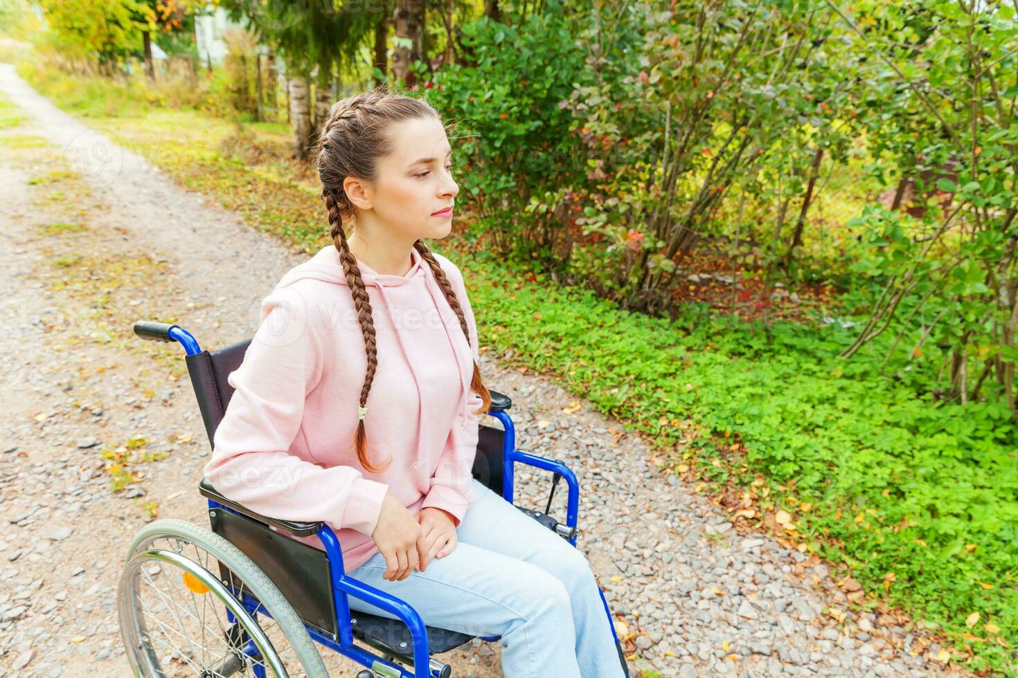 jeune femme handicapée heureuse en fauteuil roulant sur la route dans le parc de l'hôpital en attente de services aux patients. fille paralysée dans une chaise invalide pour personnes handicapées en plein air dans la nature. notion de réhabilitation. photo