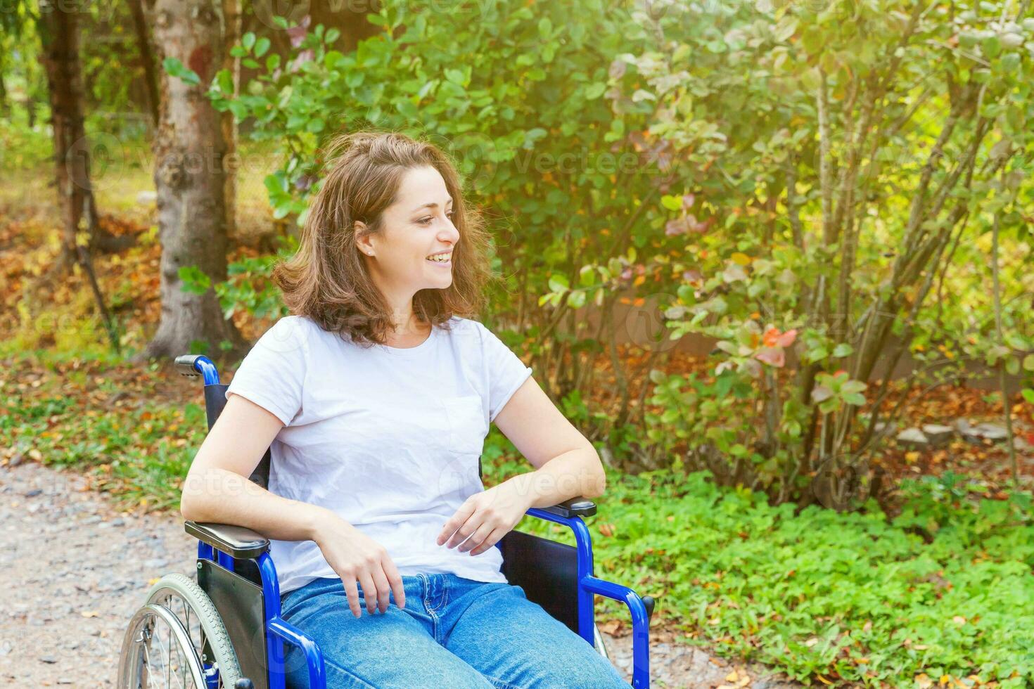 jeune femme handicapée heureuse en fauteuil roulant sur la route dans le parc de l'hôpital en attente de services aux patients. fille paralysée dans une chaise invalide pour personnes handicapées en plein air dans la nature. notion de réhabilitation. photo