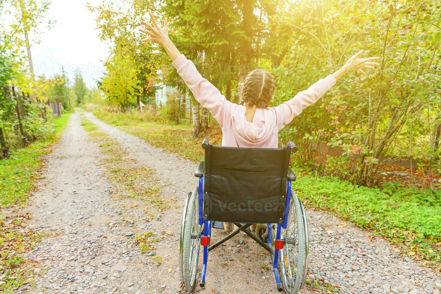 jeune femme handicapée heureuse en fauteuil roulant sur la route dans le parc de l'hôpital en profitant de la liberté. fille paralysée dans une chaise invalide pour personnes handicapées en plein air dans la nature. notion de réhabilitation. photo