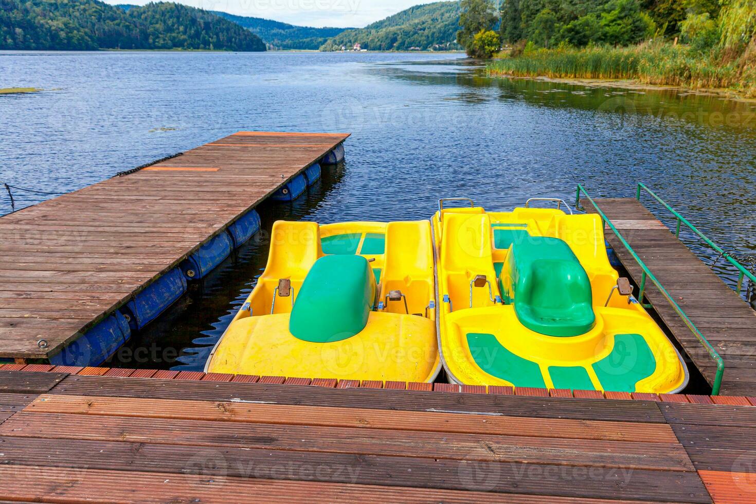 Station de pédalos ou pédalos catamarans. vélos à eau jaune verrouillés au quai du quai de la marina du lac le jour d'été ensoleillé. activité de loisirs d'été à l'extérieur. photo