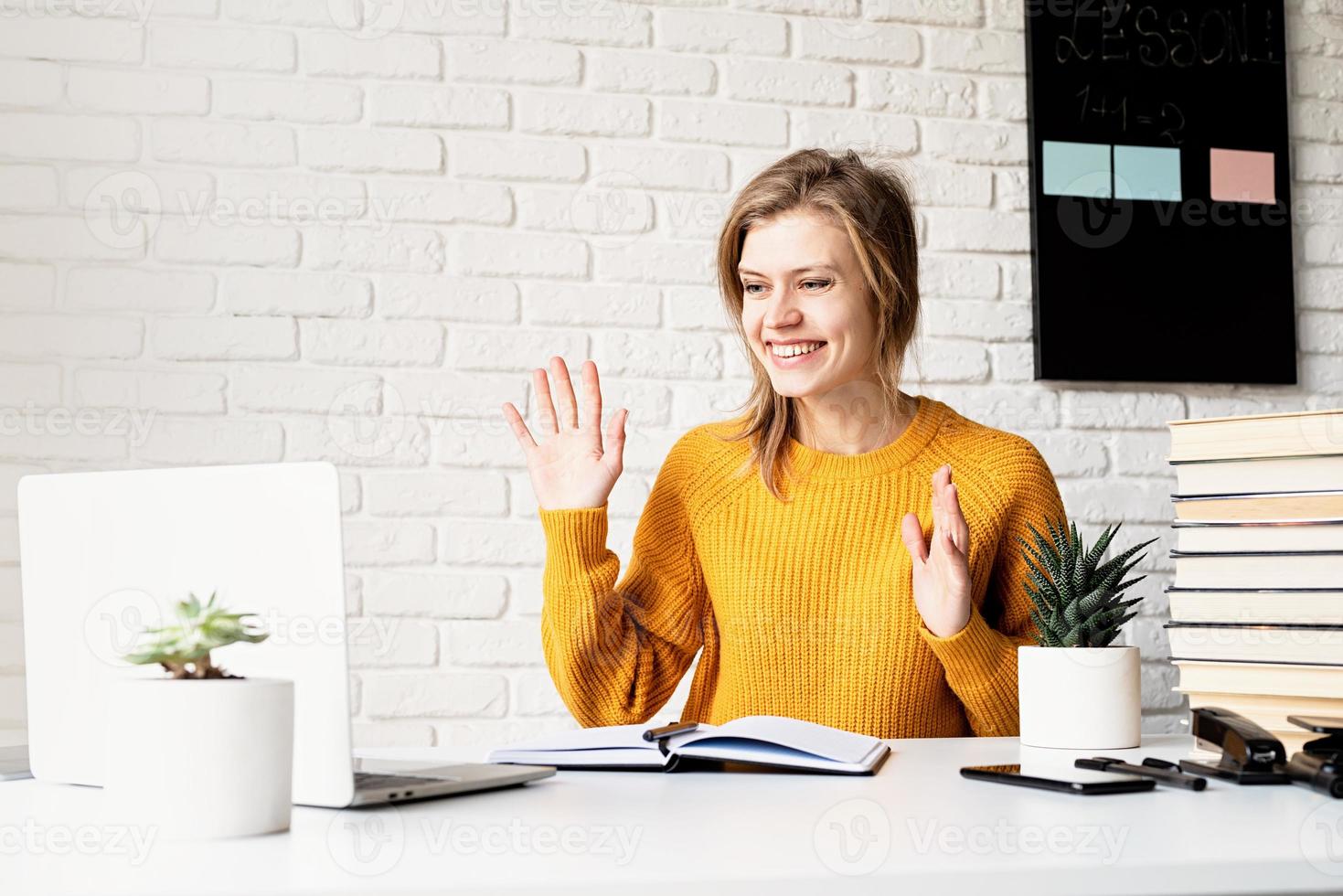 jeune femme souriante en pull jaune étudiant en ligne à l'aide d'un ordinateur portable photo