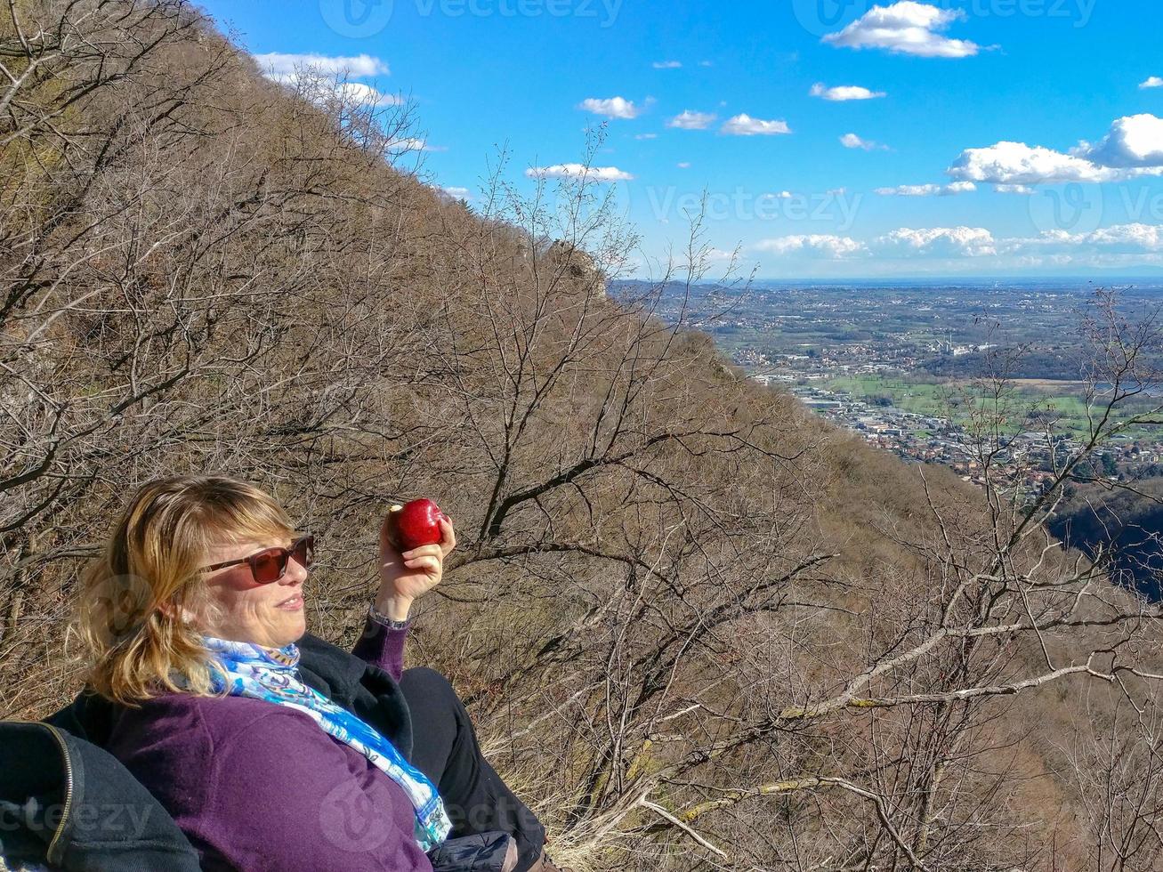 femme aux cheveux blonds au repos mangeant une pomme au sommet d'une montagne photo