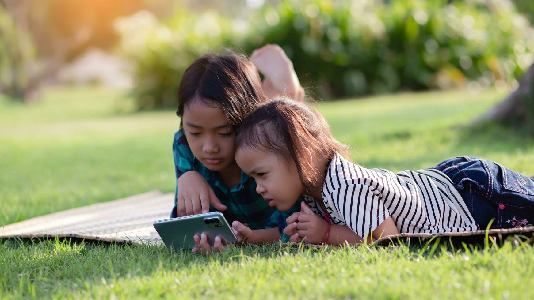 deux Jeune les filles mensonge sur le pelouse à la recherche à leur Téléphone (s, été, d'or heure, le coucher du soleil. sstkhome photo