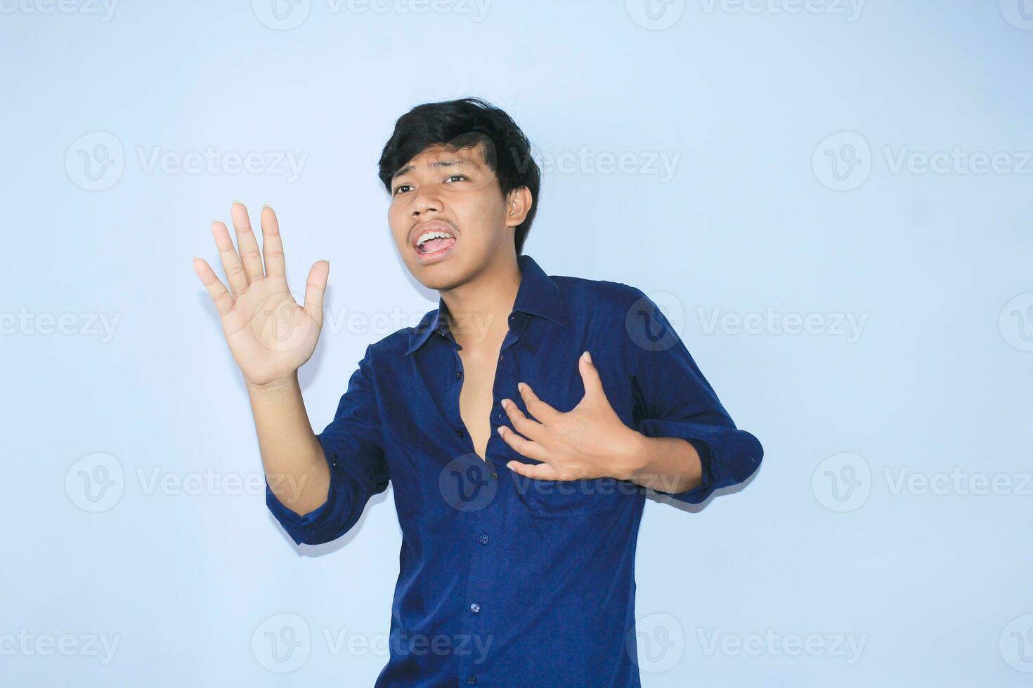 asiatique homme est en hurlant et tenir le sien poitrine après avoir douloureux cœur attaque avec mains élevé porter ouvert marine chemise photo