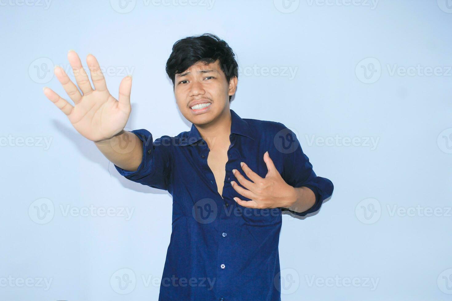 effrayé asiatique homme est élever le sien mains comme Arrêtez panneaux geste et tenir le sien poitrine sentiment douleur de cœur attaque porter ouvert chemise photo