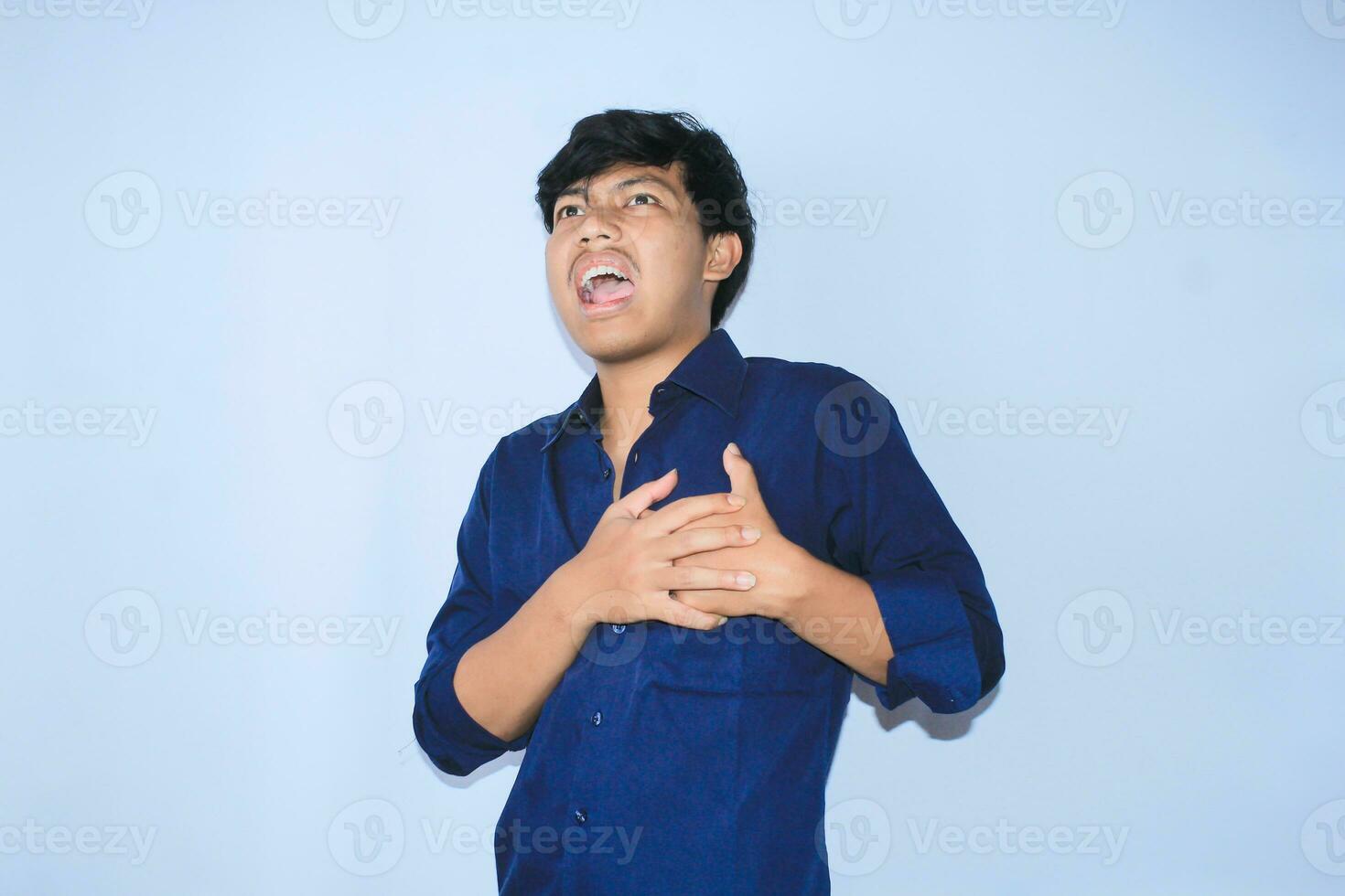 asiatique homme Bureau ouvrier en hurlant et émouvant le sien poitrine Souffrance de cœur attaque douleur portant marine chemise, isolé blanc photo