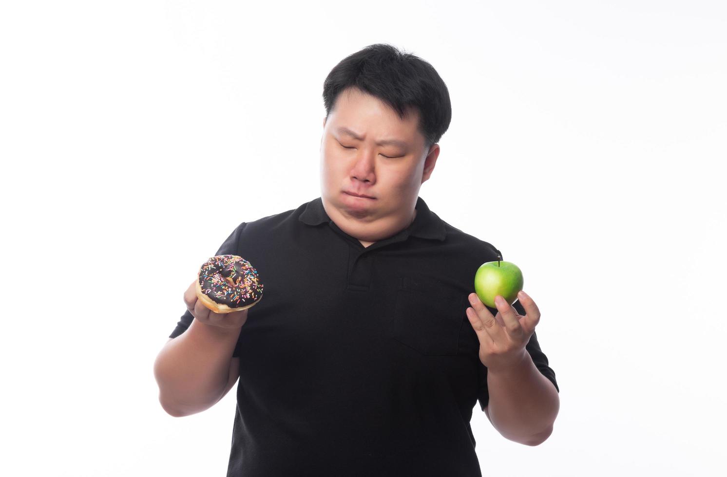 homme asiatique choisissant entre des beignets au chocolat et une pomme verte photo