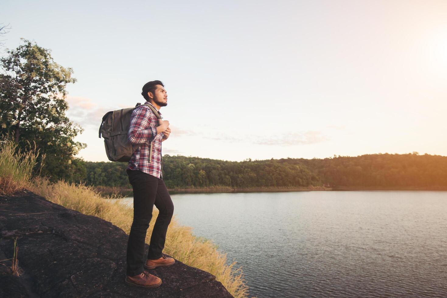 randonneur hipster homme debout sur le rocher et profitant du coucher de soleil sur le lac. photo