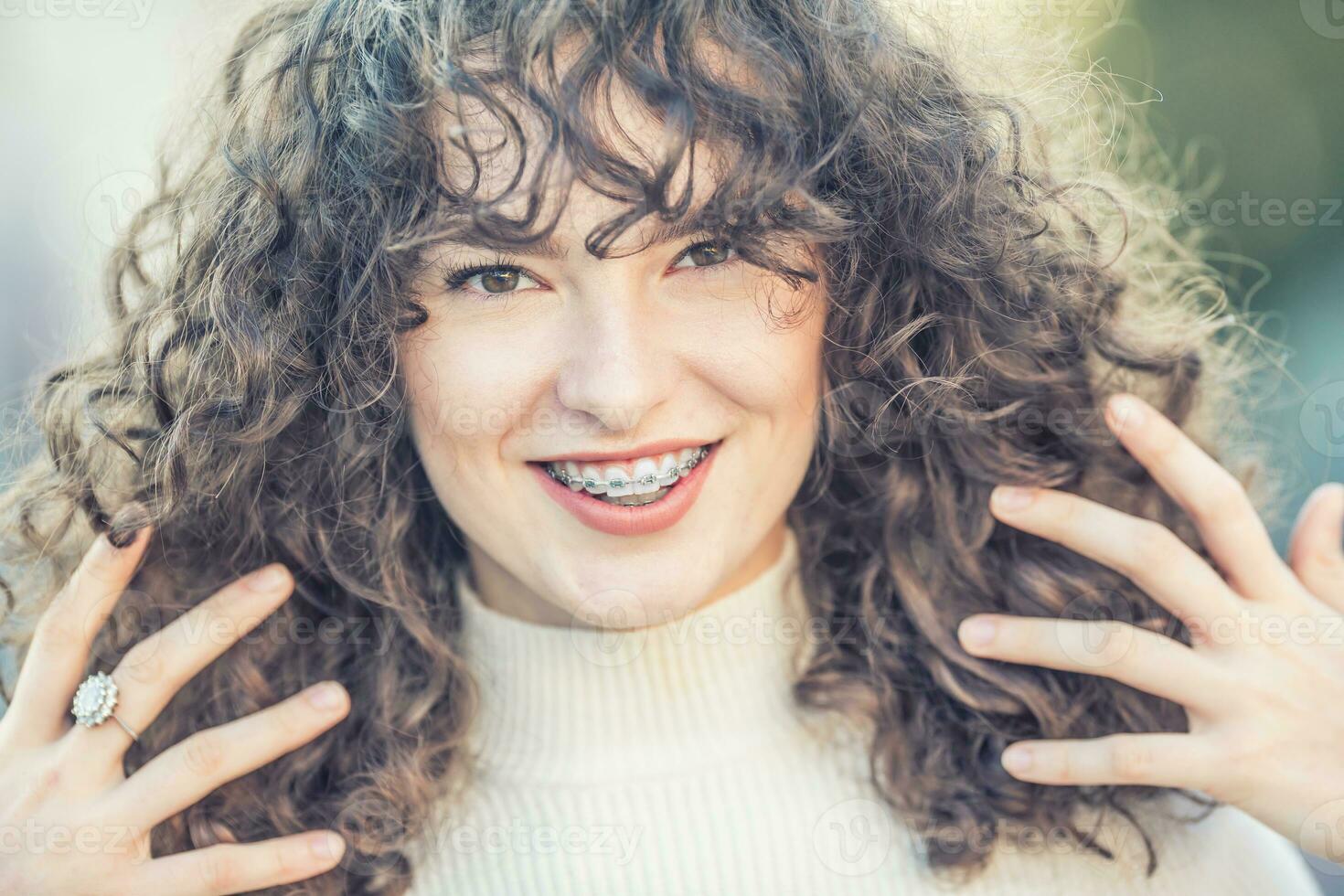 portrait de une content souriant Jeune femme avec dentaire un appareil dentaire et et frisé cheveux photo