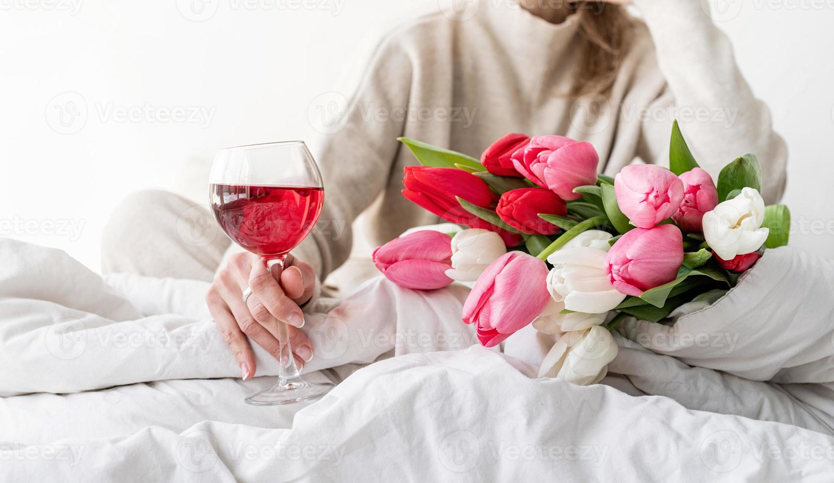 femme assise sur le be tenant un verre de vin et des fleurs de tulipes photo