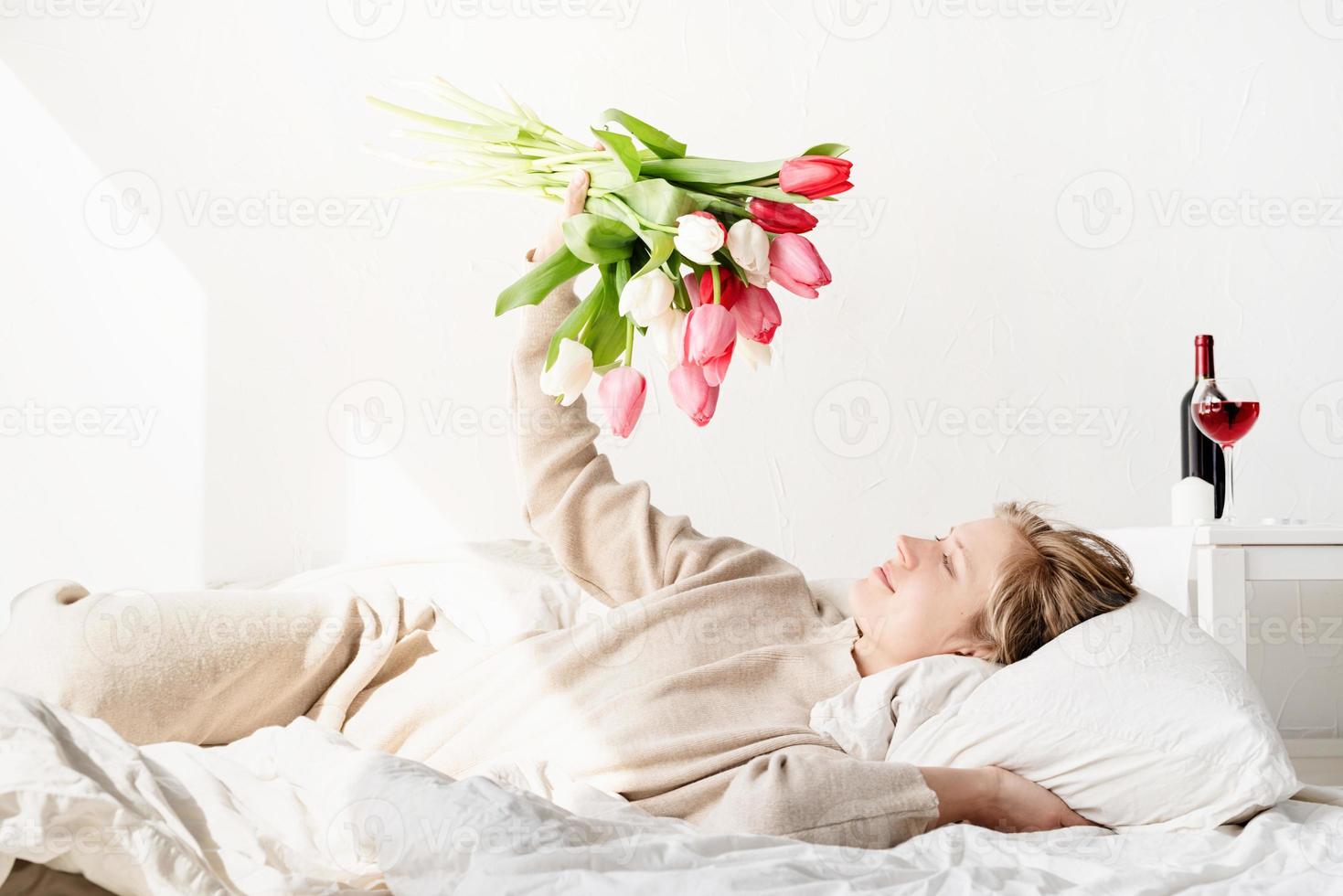 Femme allongée dans le lit en pyjama tenant un bouquet de fleurs de tulipes photo