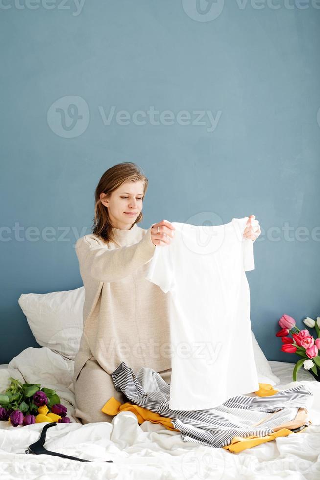 Jeune femme organisant des vêtements assis sur le lit à la maison photo