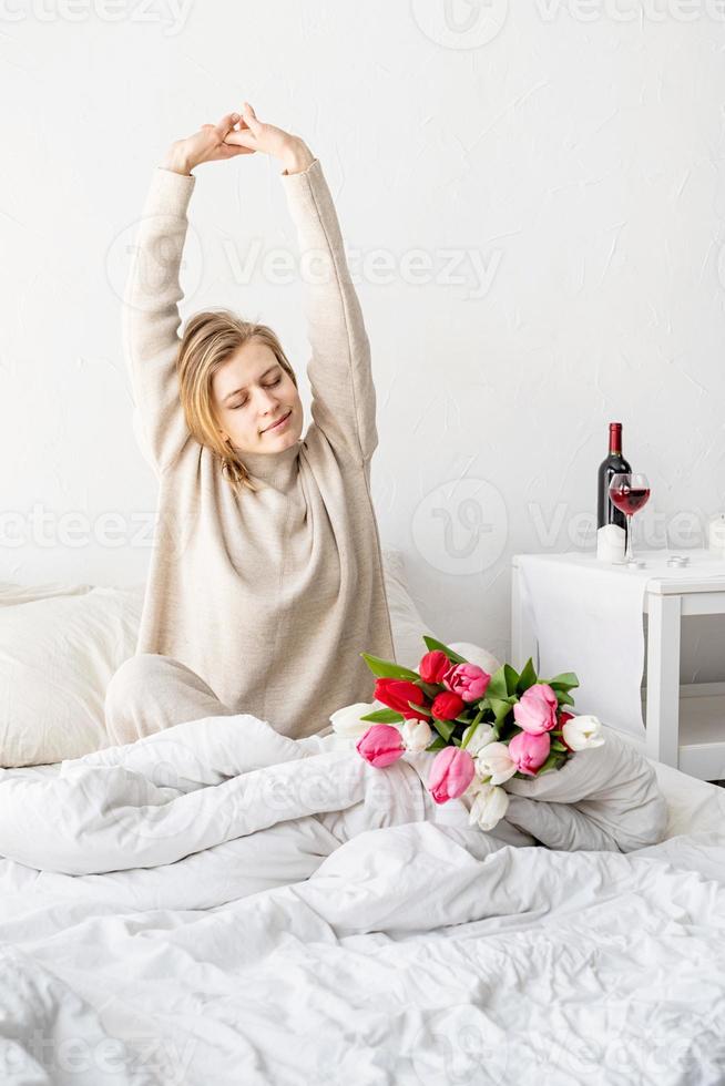 femme heureuse assise sur le lit en pyjama qui s'étend photo