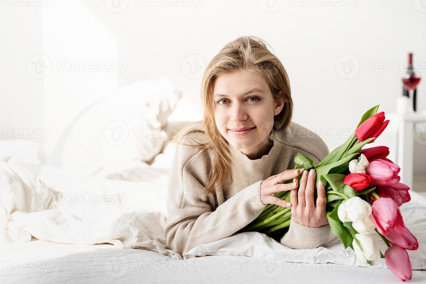 Femme allongée dans le lit en pyjama tenant un bouquet de fleurs de tulipes photo