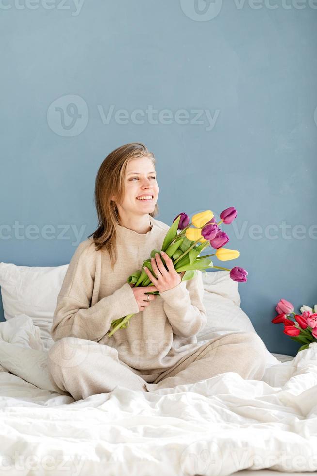 femme tenant un bouquet de fleurs de tulipes, fond de mur bleu photo