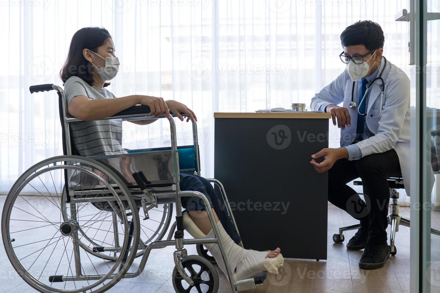 un médecin asiatique examine un patient en fauteuil roulant à cause d'une blessure à la jambe photo