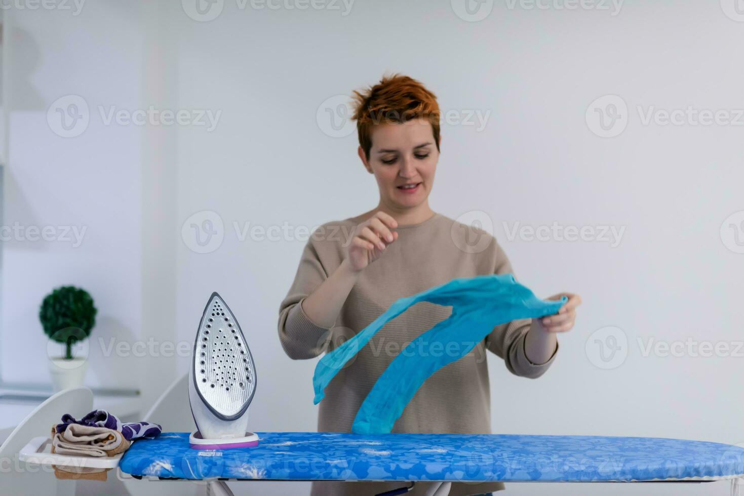 femme aux cheveux rouges repassant des vêtements à la maison photo