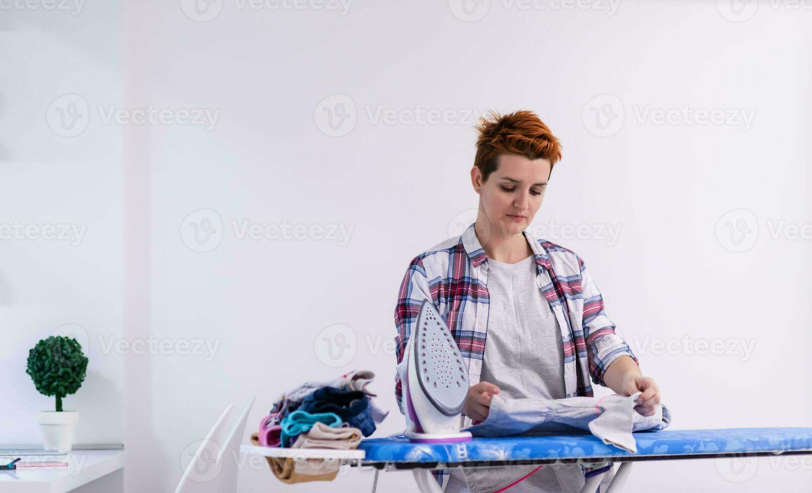 femme aux cheveux rouges repassant des vêtements à la maison photo