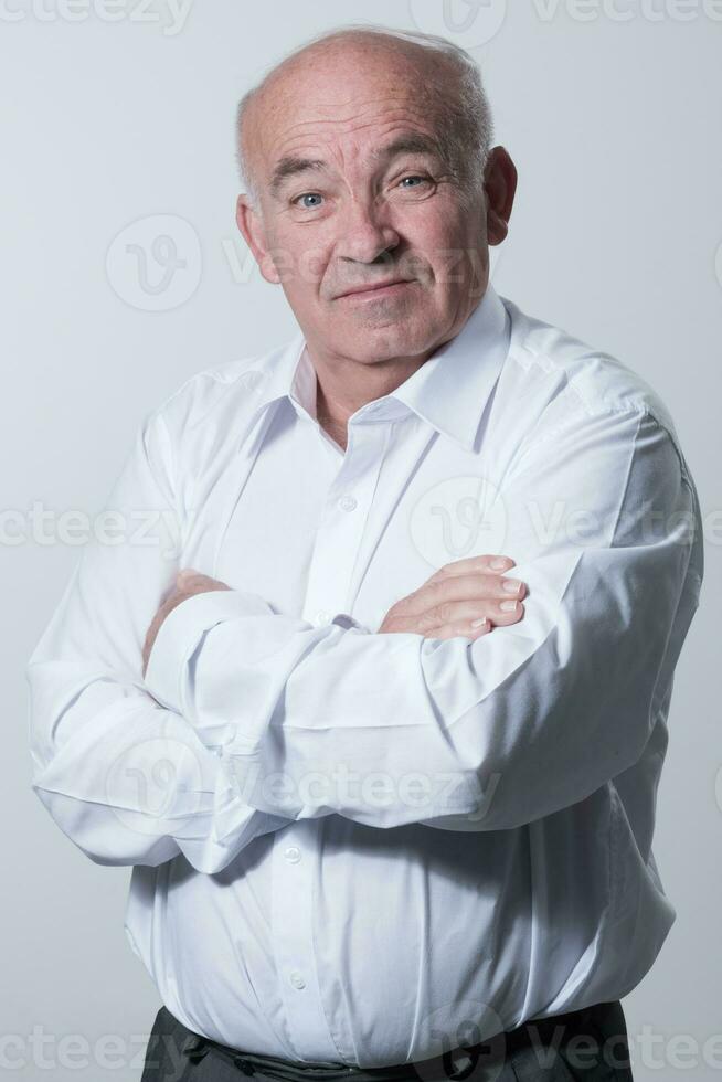 sur de soi Sénior homme dans blanc chemise traversée mains sur poitrine et à la recherche à caméra tandis que permanent contre gris Contexte. soi sur de soi Sénior isolé blanc studio tirer. photo