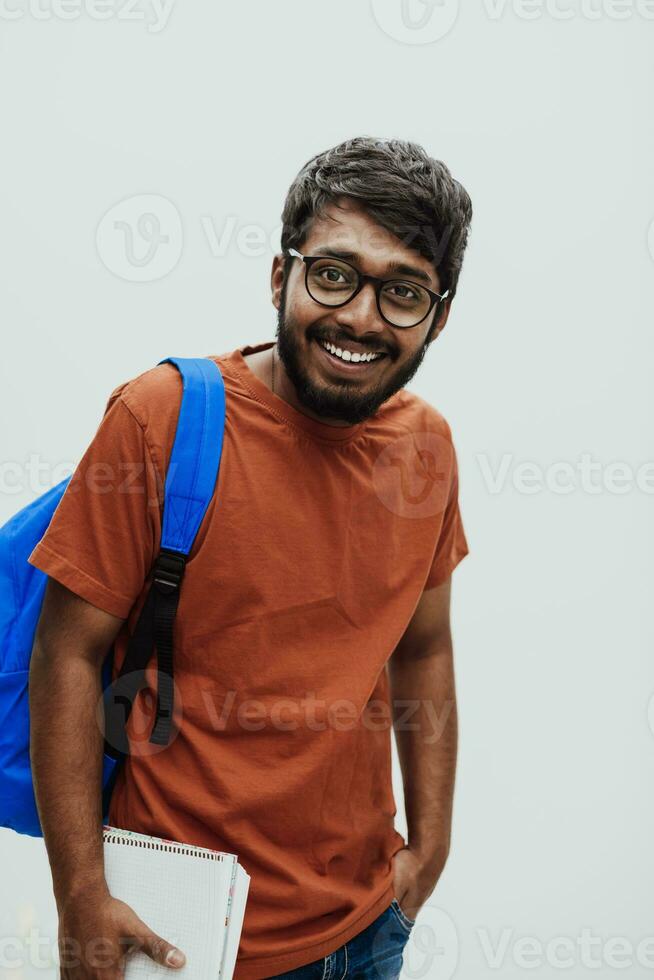 Indien étudiant avec bleu sac à dos, des lunettes et carnet posant sur gris Contexte. le concept de éducation et scolarité. temps à aller retour à école photo