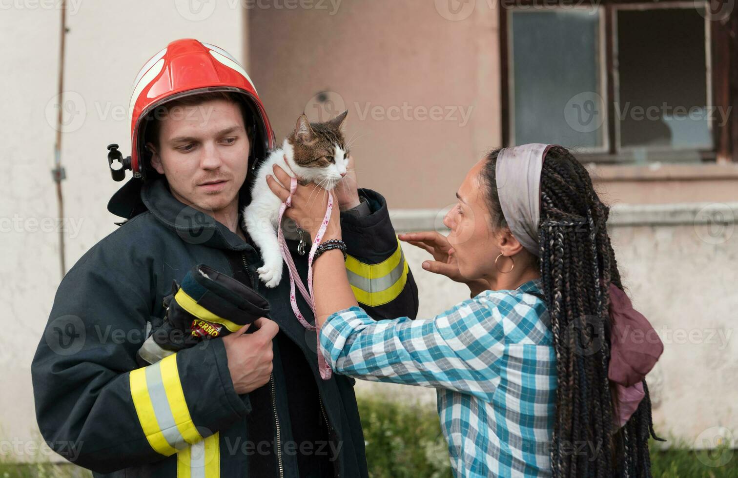 fermer portrait de héroïque pompier dans protecteur costume et rouge casque détient enregistré chat dans le sien bras. sapeur pompier dans Feu combat opération. photo