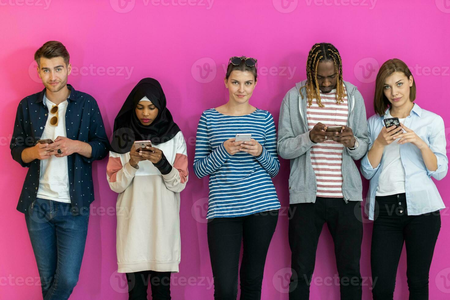 diverse adolescents en utilisant mobile dispositifs tandis que posant pour une studio photo dans de face de une coloré Contexte