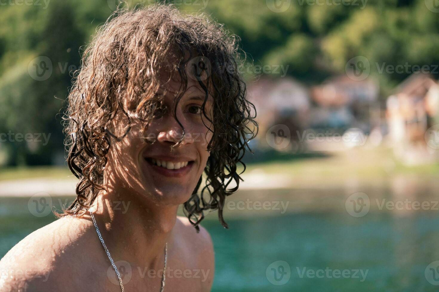 portrait de une Jeune adolescent garçon avec frisé humide cheveux près le rivière ayant amusement avec copains à une été faire la fête. photo