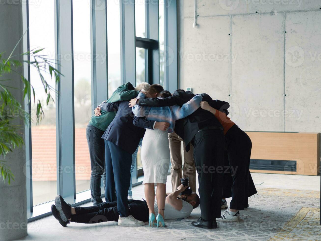 dans les coulisses. le photographe prend une photo de une diverse groupe de les hommes d'affaires dans une moderne Bureau qui étreinte chaque autre dans une cercle