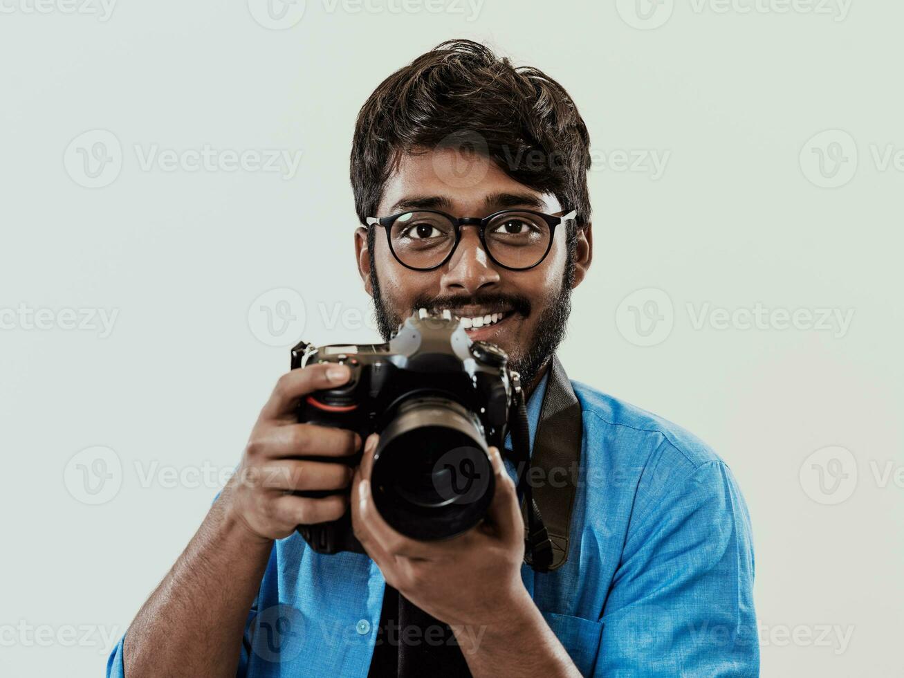 professionnel photographe ayant dslr caméra prise photo.indien homme la photographie passionné prise photo tandis que permanent sur bleu Contexte. studio coup