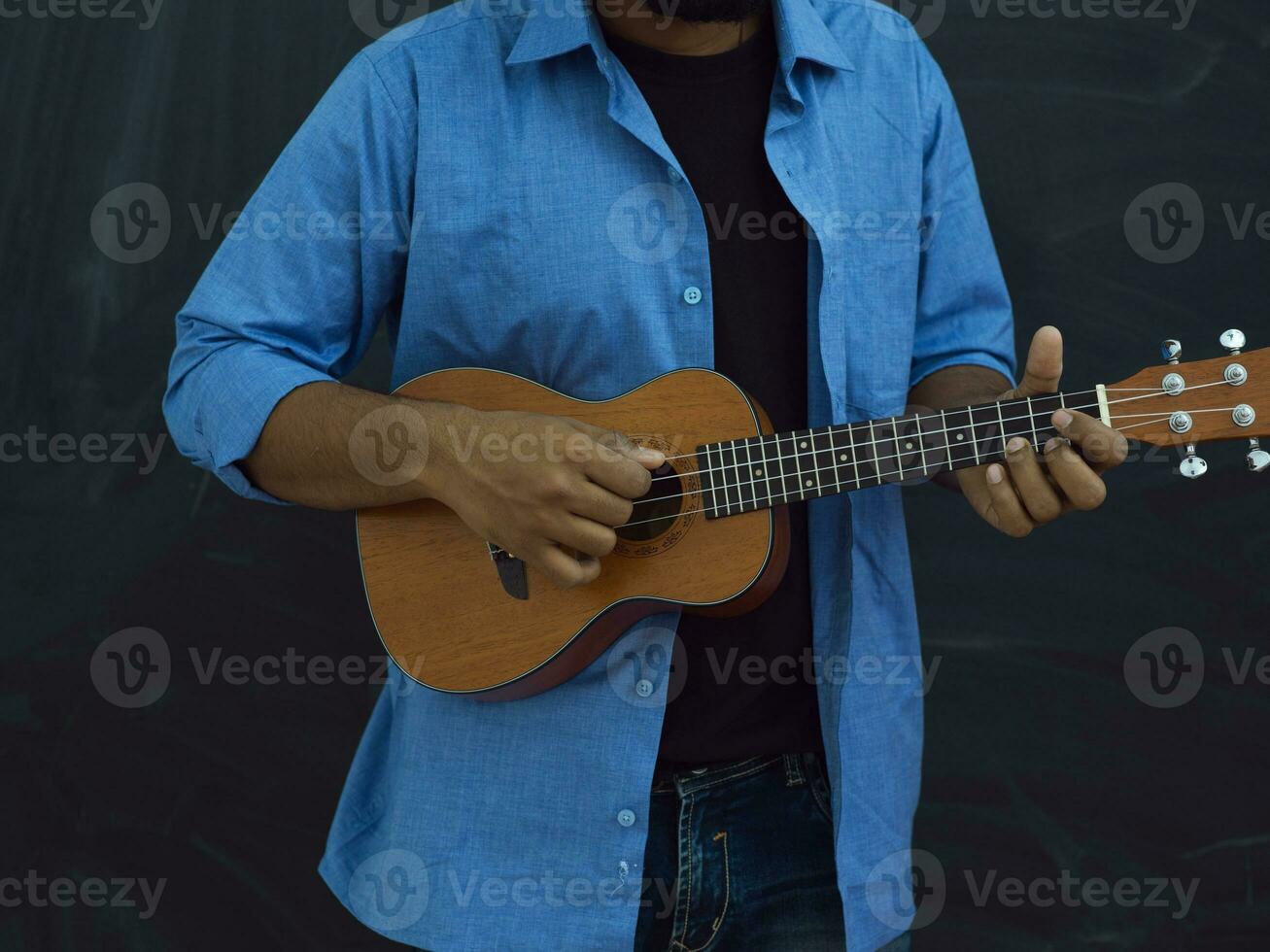 Indien Jeune homme dans une bleu chemise et des lunettes en jouant le guitare dans de face de le école tableau noir photo