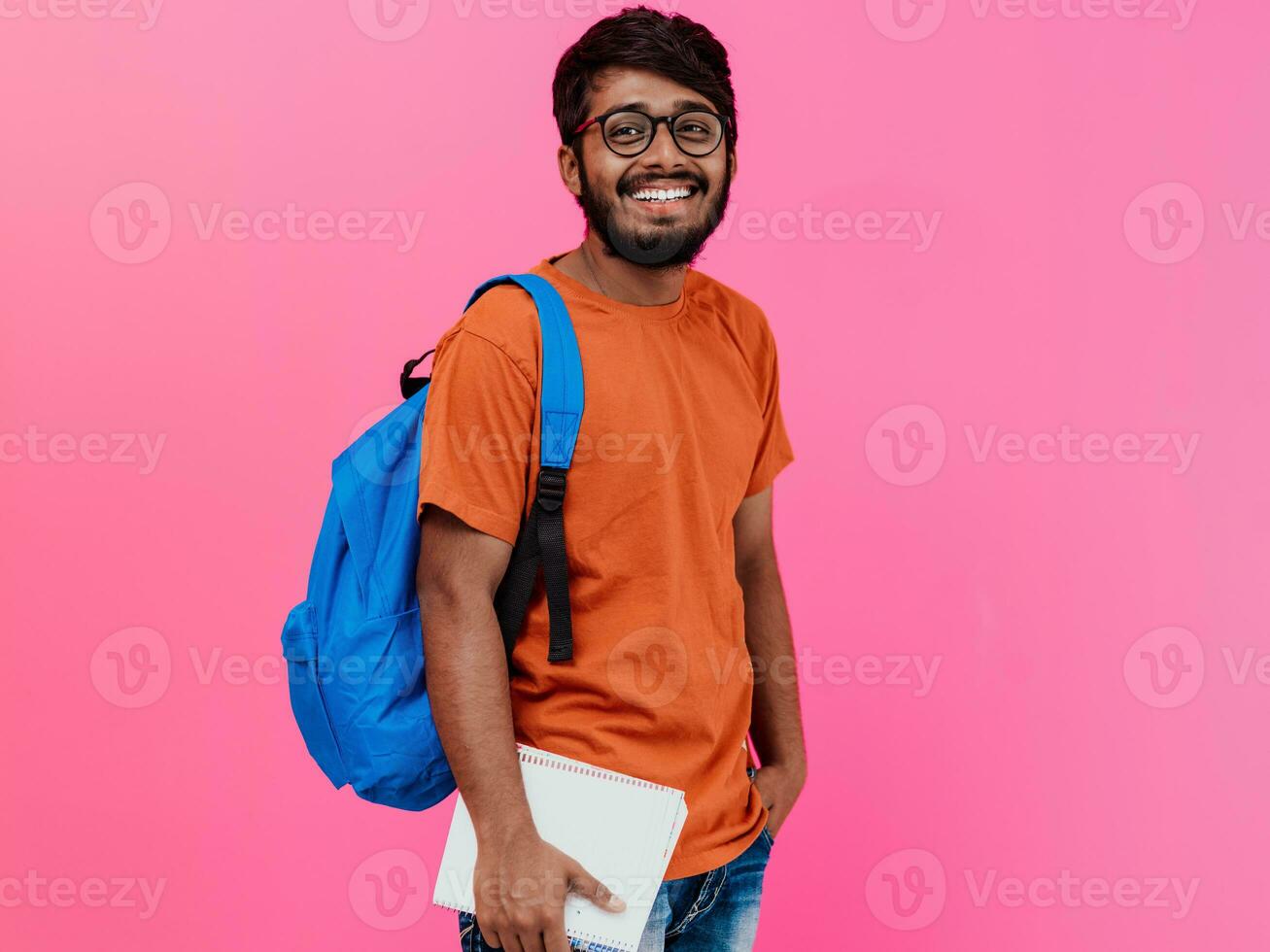 Indien étudiant avec bleu sac à dos, des lunettes et carnet posant sur rose Contexte. le concept de éducation et scolarité. temps à aller retour à école photo