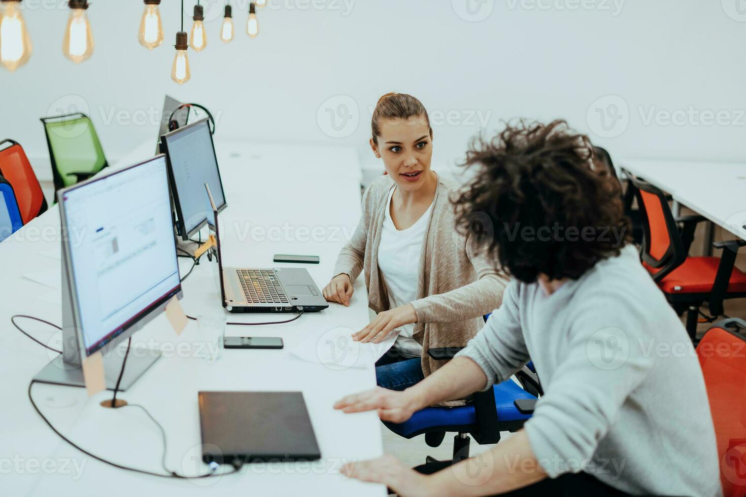 deux collègues travail sur une projet dans moderne Commencez des bureaux. gars avec afro la Coupe de cheveux et une femelle blond employé travail à le bureau. photo