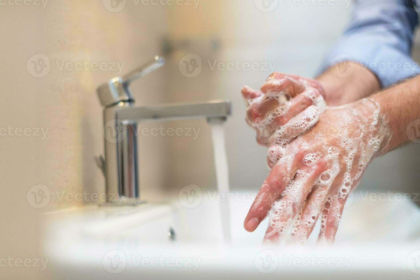 homme en utilisant savon et la lessive mains en dessous de le l'eau robinet. hygiène concept main fermer détail. photo