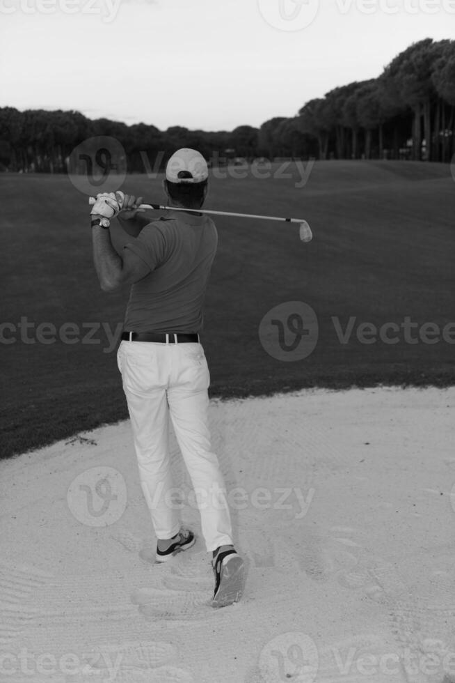 golfeur frappant un bunker de sable tourné au coucher du soleil photo