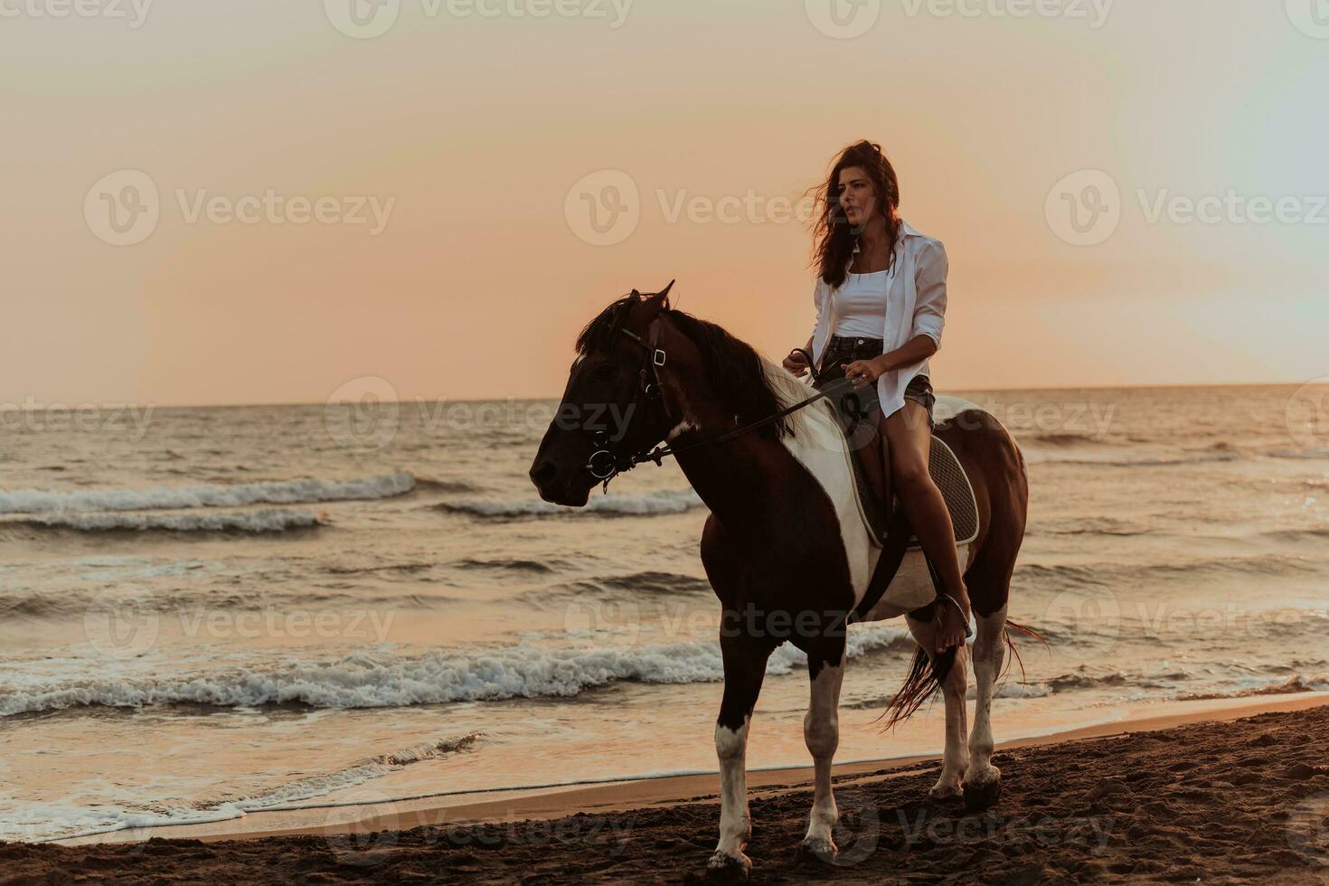 femme en vêtements d'été aime monter à cheval sur une belle plage de sable au coucher du soleil. mise au point sélective photo