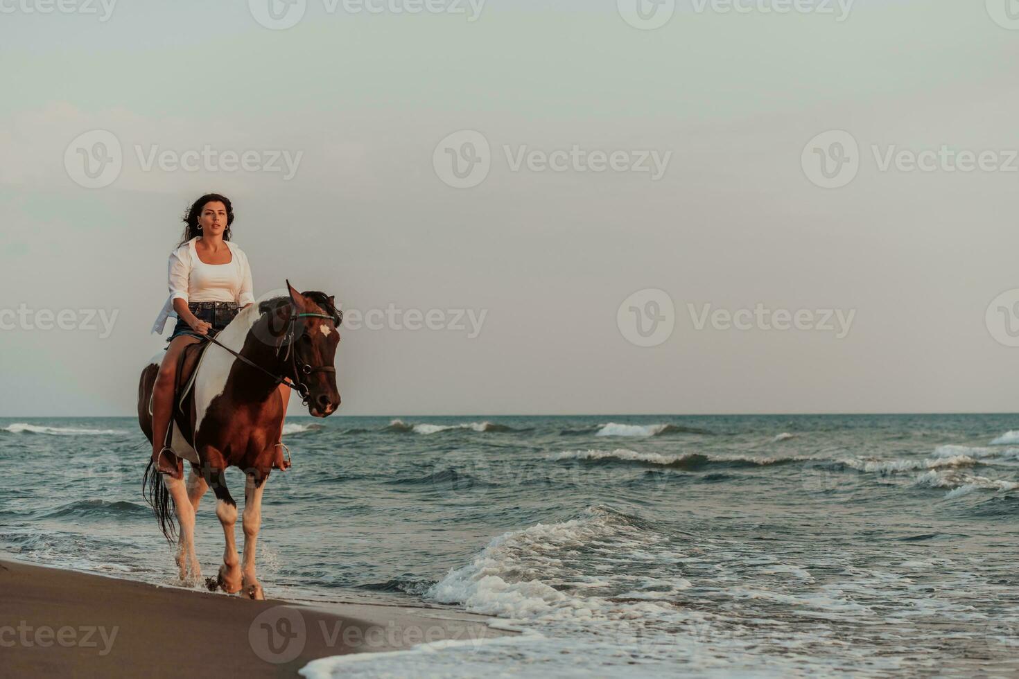 femme en vêtements d'été aime monter à cheval sur une belle plage de sable au coucher du soleil. mise au point sélective photo