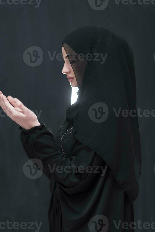 portrait de magnifique musulman femme dans à la mode robe avec hijab fabrication traditionnel prière à Dieu garde mains dans prier geste isolé sur noir Contexte photo