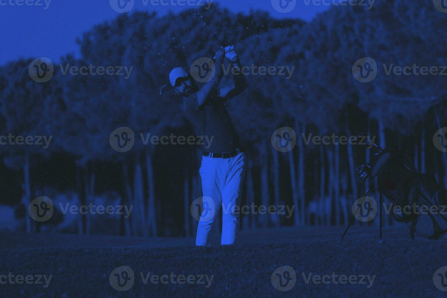 golfeur frappant un bunker de sable tourné au coucher du soleil photo