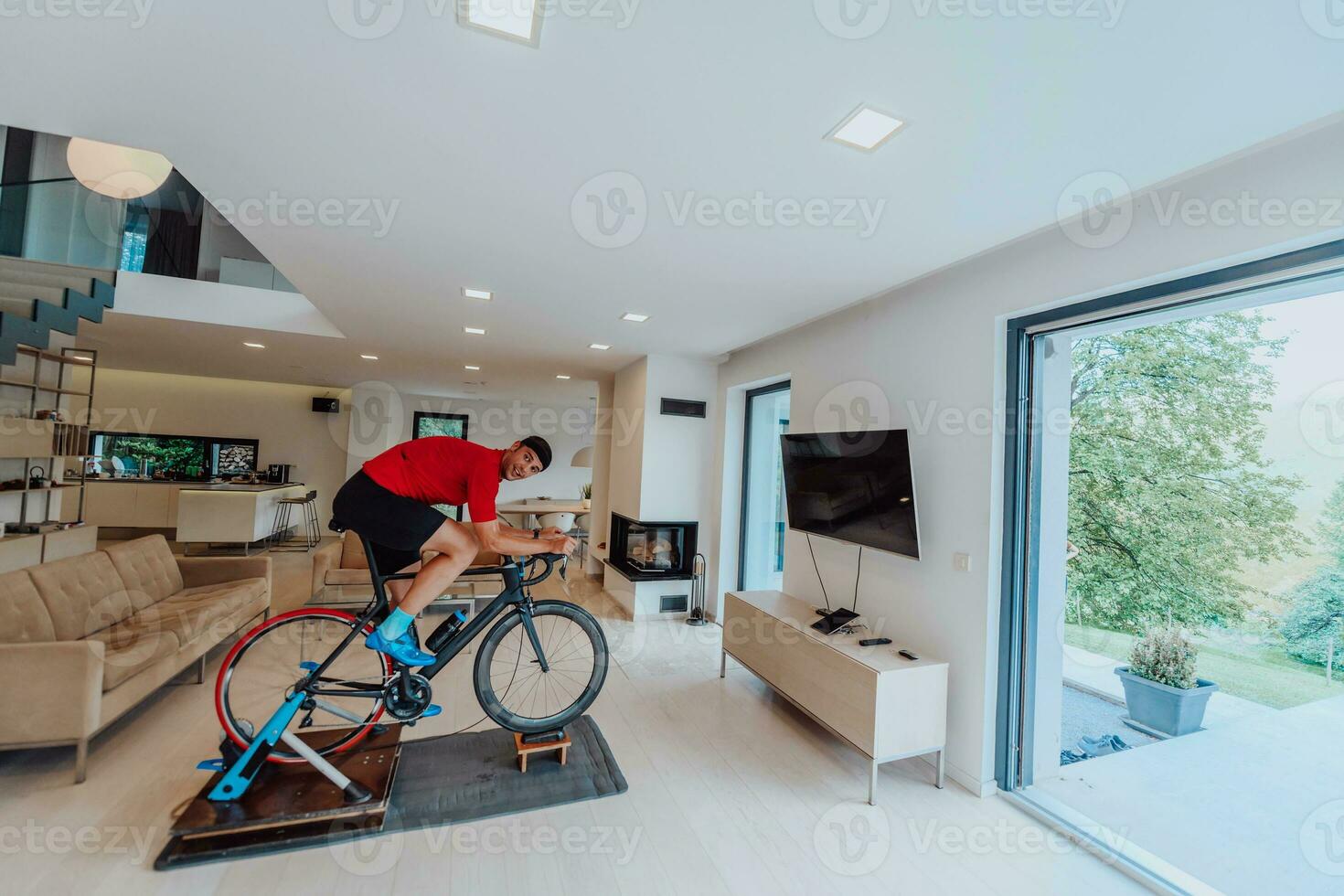 une homme équitation une triathlon bicyclette sur une machine simulation dans une moderne vivant chambre. formation pendant pandémie conditions. photo