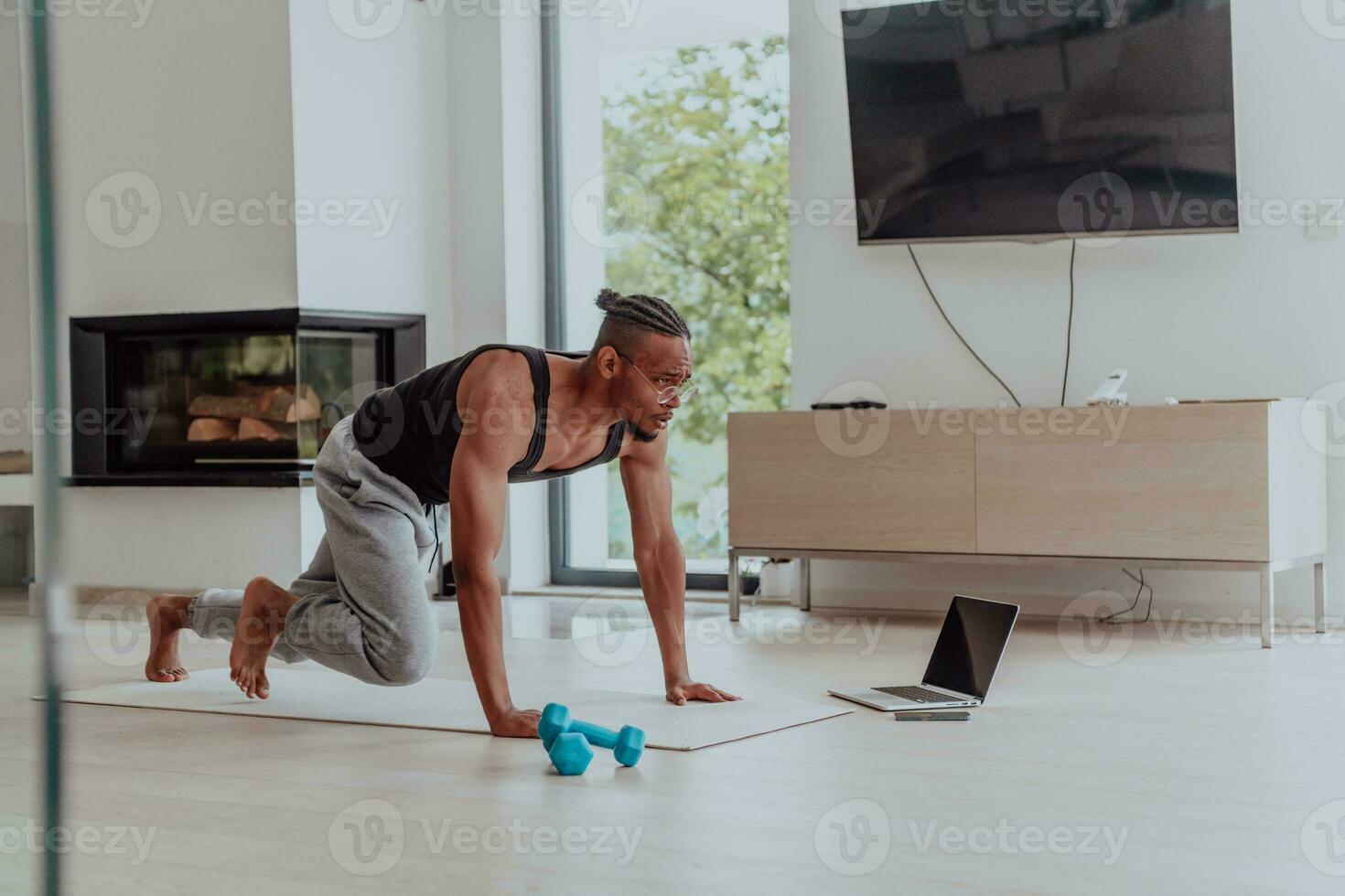 formation à maison. sportif homme Faire formation tandis que en train de regarder en ligne Didacticiel sur ordinateur portable, exercice dans vivant chambre, gratuit espace photo